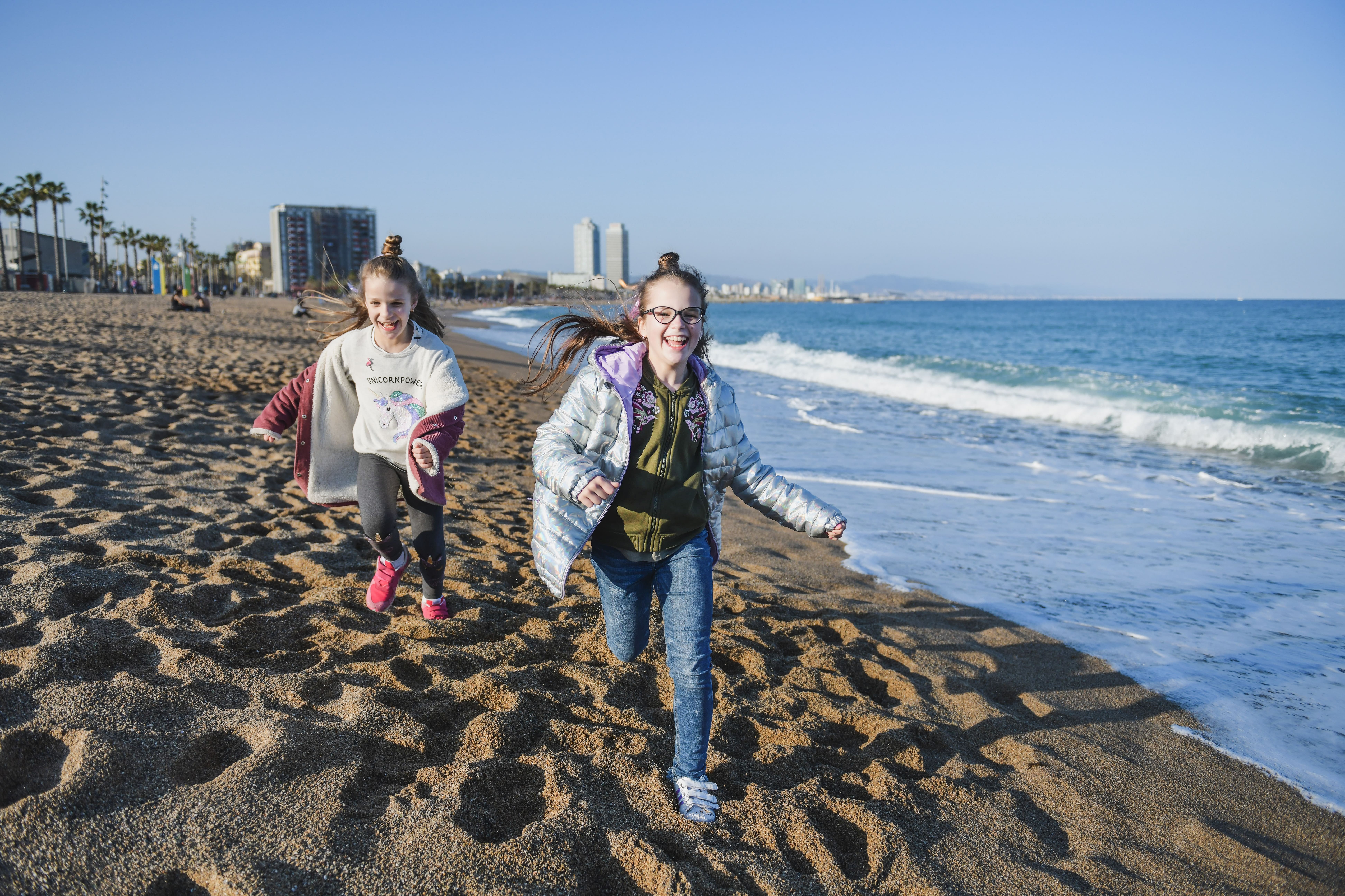two happy young girls running along the sea coast in Barcelona
